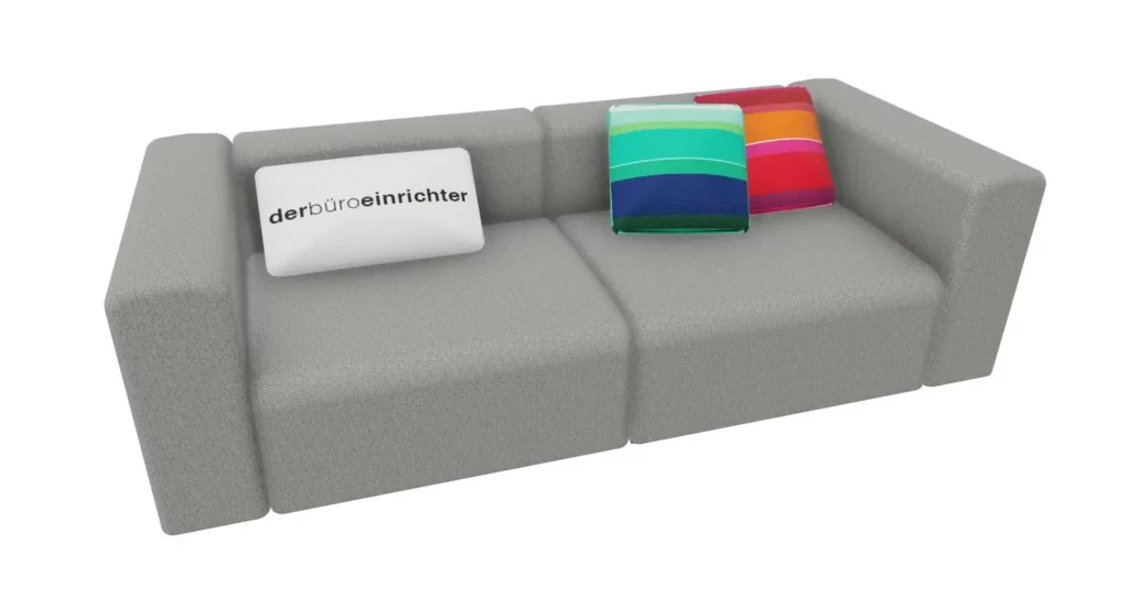 Graues Sofa mit weißem Kissen "derbüroeinrichter" und bunten Kissen in Grün- und Rottönen.