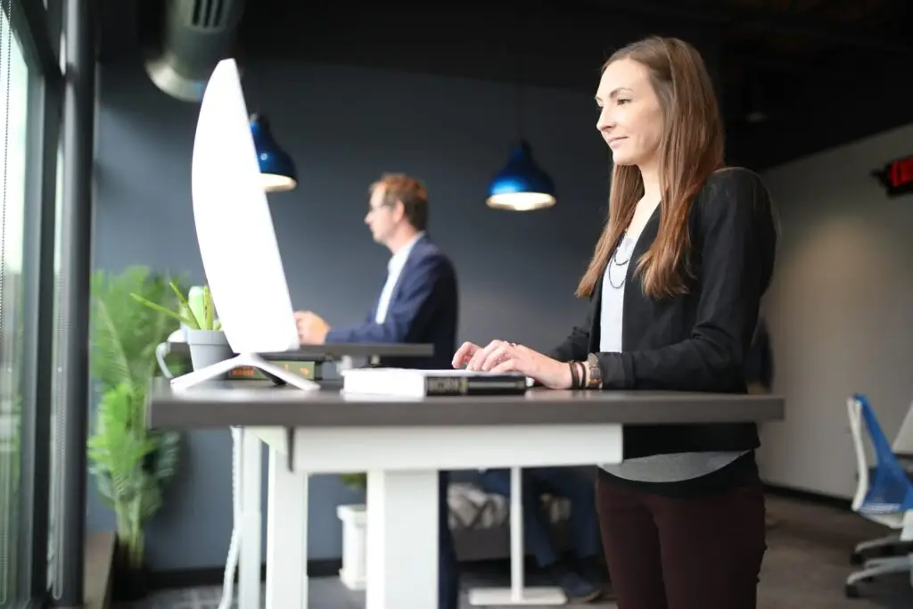 Modernes Büro mit einer Frau im Vordergrund und einem Mann im Hintergrund, arbeitend an Stehpulten.