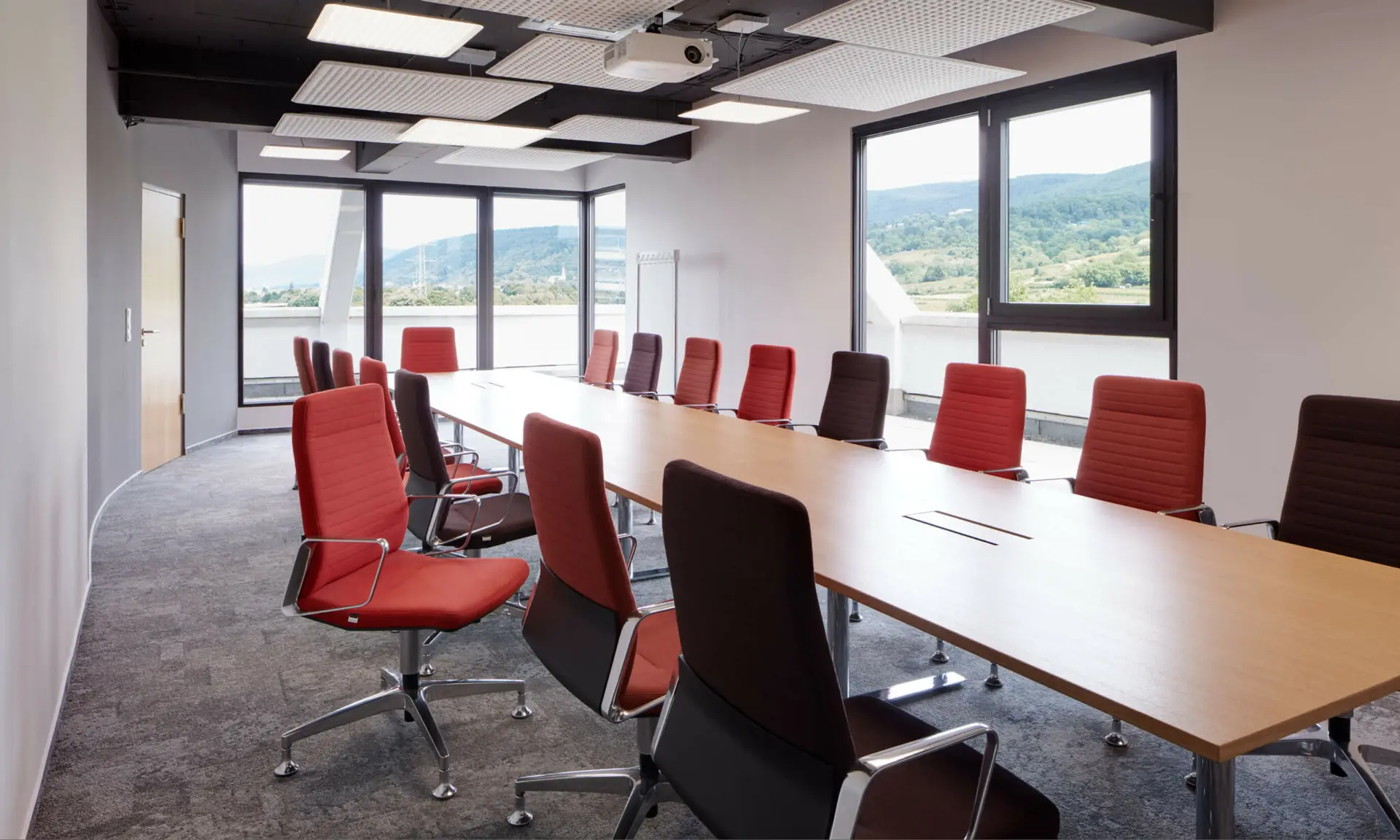 Moderner Konferenzraum mit großem Tisch, gepolsterten Stühlen und Ausblick auf Landschaft.