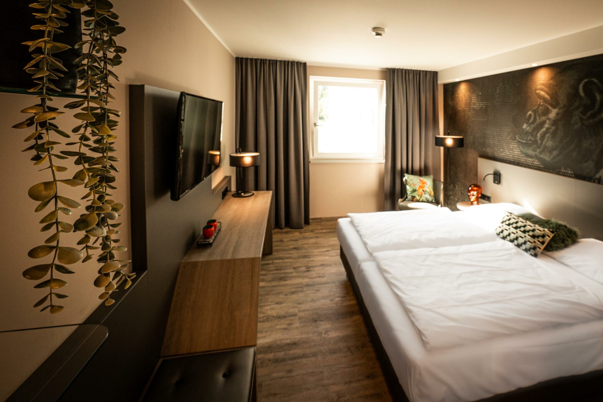 Modernes Hotelzimmer mit Doppelbett, Schreibtisch, Flachbildfernseher und Wanddekor hinter dem Bett