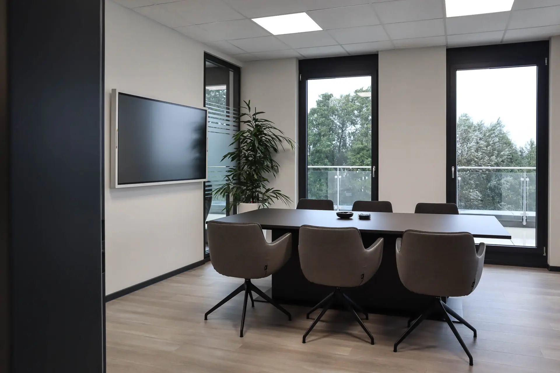 Besprechungszimmer mit rechteckigem Tisch, sechs Stühlen, Flachbildschirm und Blick ins Grüne.